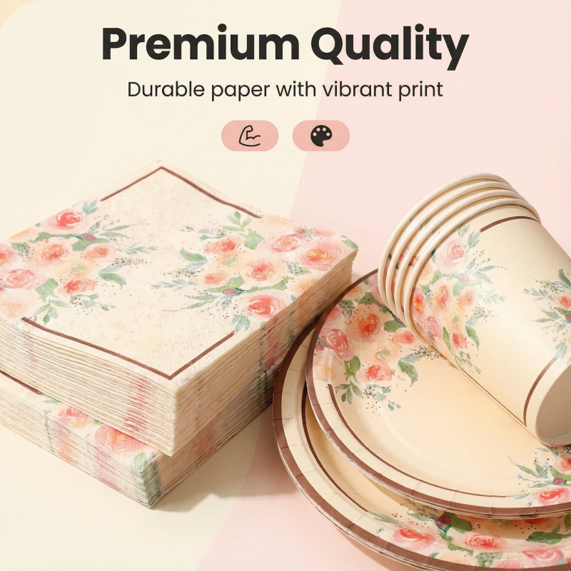 Textured disposable paper party tableware set with pink rose print and gold foil borders, including napkins, plates, and cups, styled with party confetti and balloons
