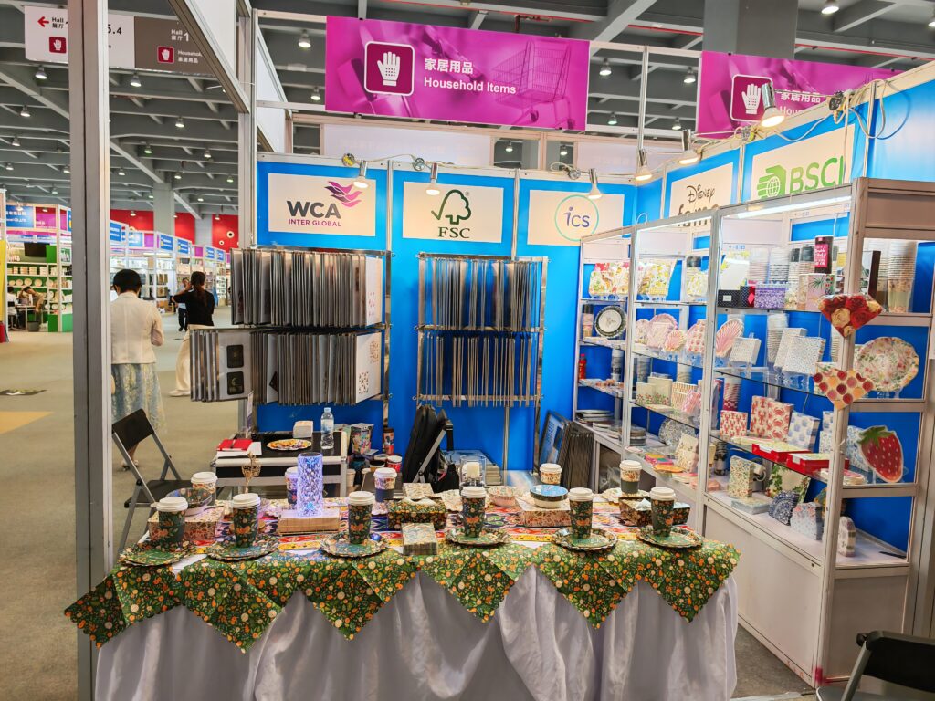 Cedar Paper trade show booth at a household products exhibition, showcasing custom printed paper napkins, plates, and cups, with certifications like FSC, BSCI, and WCA displayed.